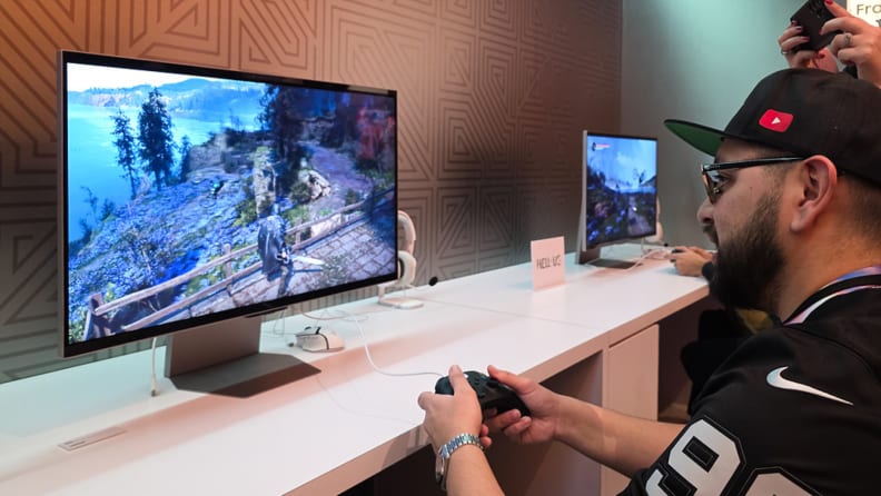 A gamer plays an action game on a Samsung 3D gaming monitor at a demo station, using a controller while the depth-enhanced display fills the screen.