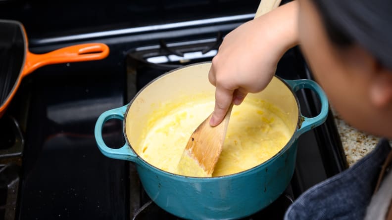 A person mixing pumpkin pie filling in a pot on a stove.