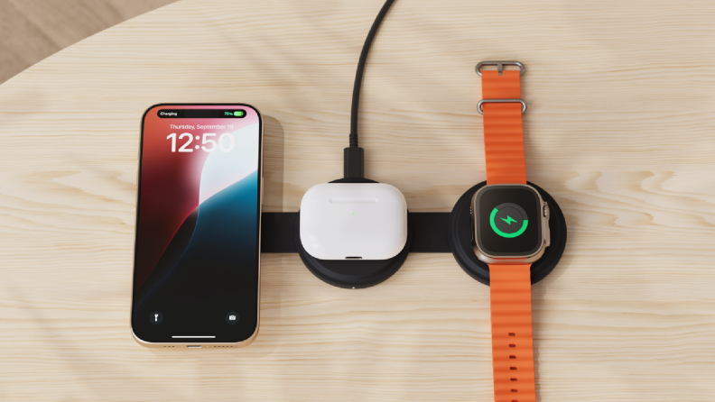 A sleek wireless charging station on a wooden surface, simultaneously powering an iPhone, a pair of AirPods, and an Apple Watch with an orange band.