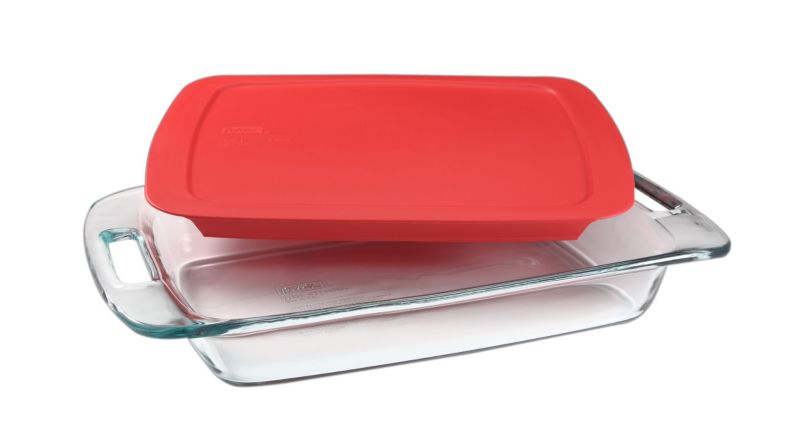 An image of a glass Pyrex baking dish with a red lid sat slightly askew on top of it, on a white background.