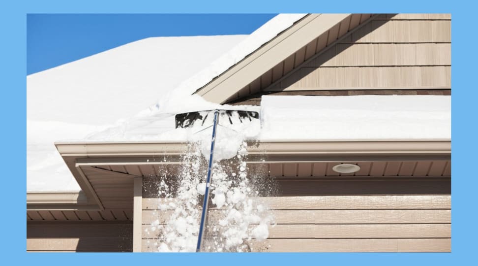 A person clears snow from their home with a roof rake.