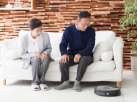 Older couple sitting on couch together watching robot vacuum clean.