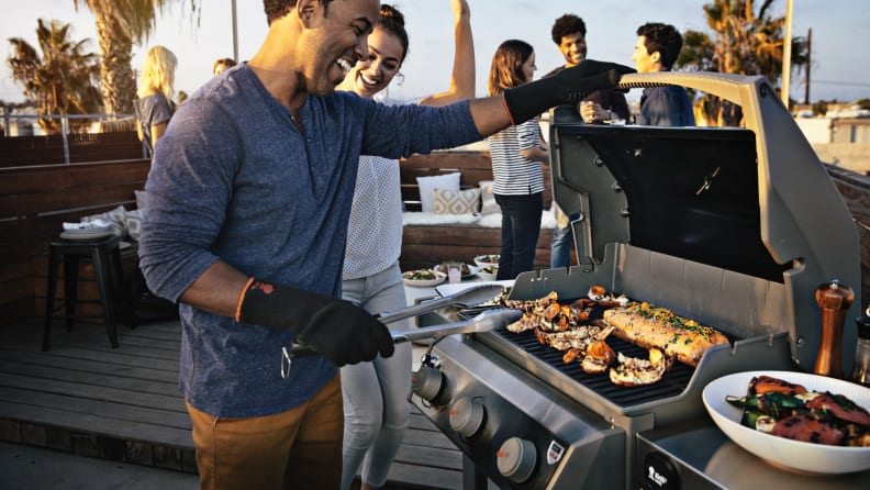 Man grilling meat on an open grill next to his friends.