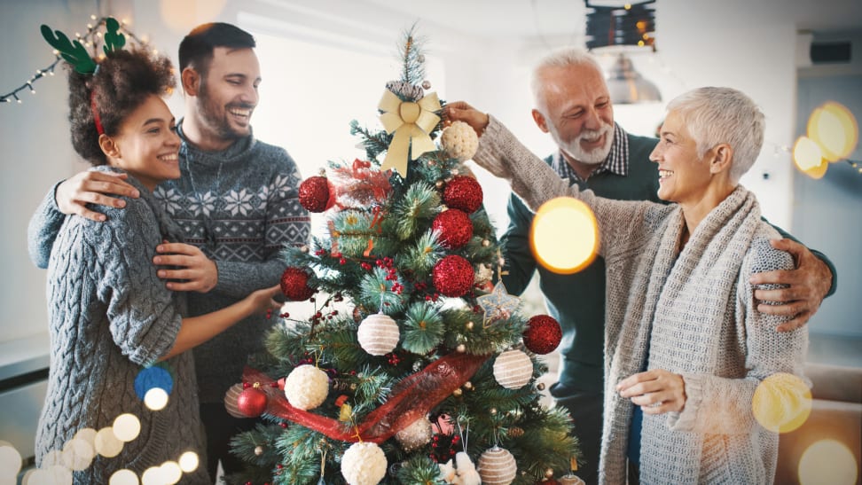 Four people decorate a Christmas tree with ornaments.