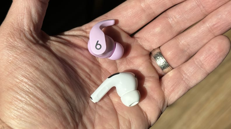 A purple Beats Fit Pro and Apple AirPods Pro 2 earbud held in the palm of a hand.