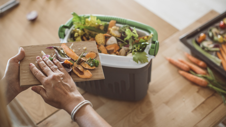 A person adds food clippings to a compost pile.