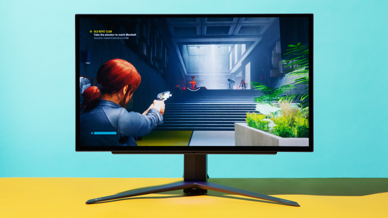 Looking at a gaming monitor on a blue background, onscreen is a woman shooting a gun
