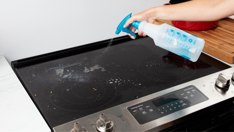 Person using spray bottle to clean oven range surface.