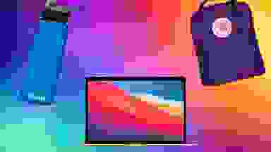 Rainbow background with a blue water bottle, Apple laptop, and small purple backpack