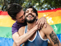Gay couple kissing in front of a pride flag