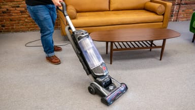 A person pushes the Hoover Swivel XL Pet upright vacuum across tan carpeting