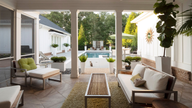 Upscale modern patio furniture with a coffee table, plants, throw pillows, and a blanket next to a pool