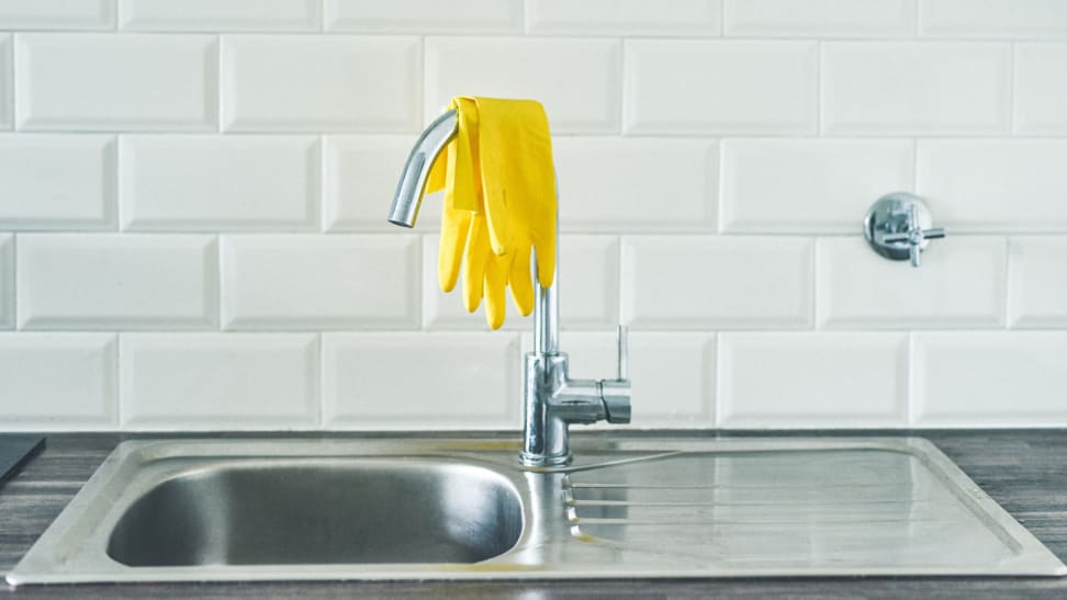 A pair of yellow rubber gloves lay on top of a faucet.