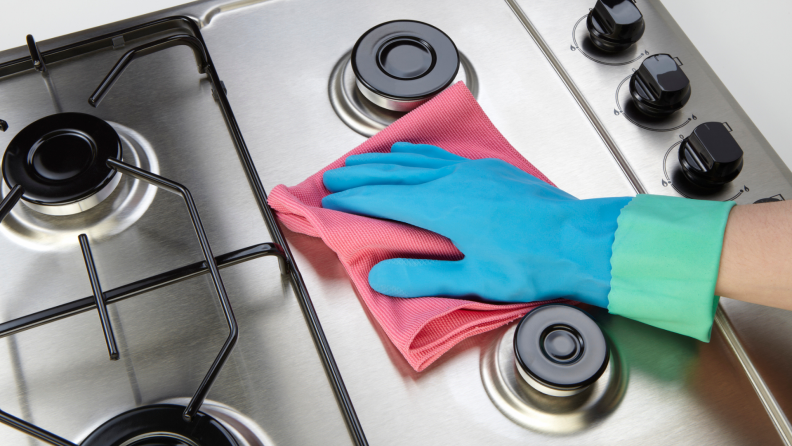 A person wipes a stainless steel stove clean.