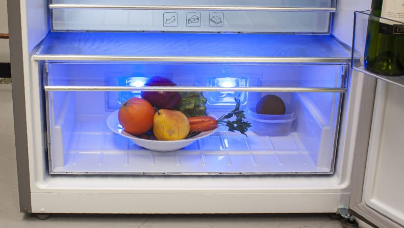 A close-up of the crisper, with a bowl of fruit inside it for scale. Behind the bowl you can see the blue LEDs, which illuminate the entirety of the drawer.
