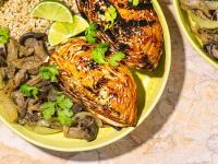 An image of a bowl of rice, mushrooms, and grilled, spicy cabbage on a green plate, garnished with lime wedges.