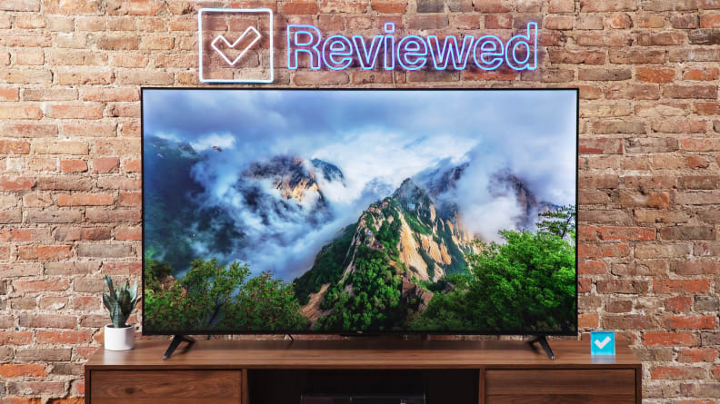 The TCL S4 on a home theater credenza in front of a brick wall with a neon sign that says Reviewed.