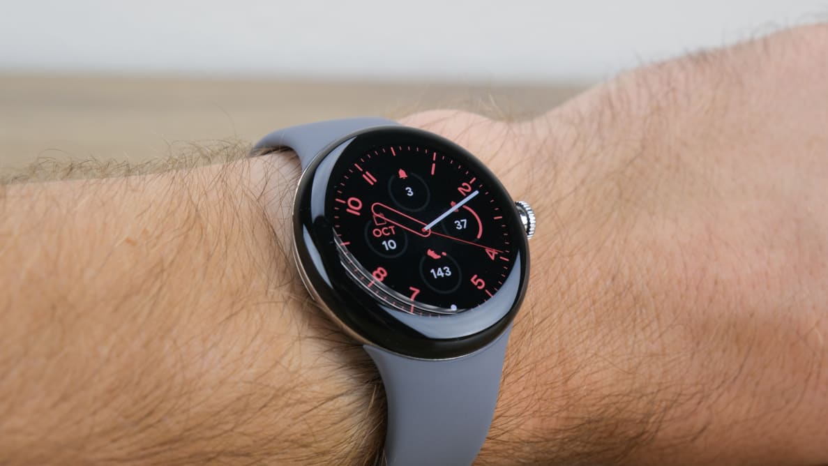 A stylish, round watch sits on a wrist with red digital face and a gray band.