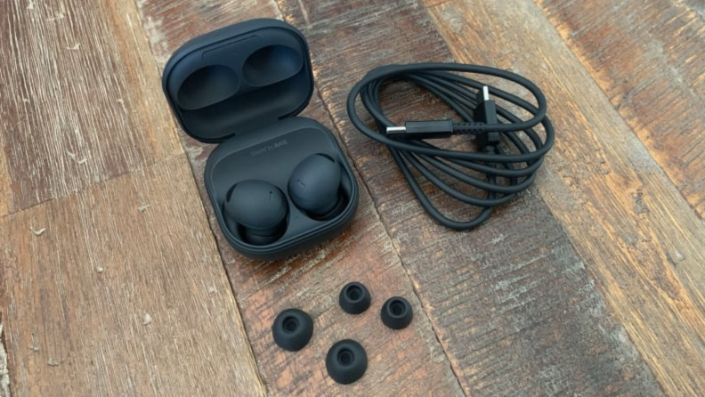 The Samsung Galaxy Buds 2 Pro in their clamshell case with a charging cable and different ear tips on a reclaimed wooden table.