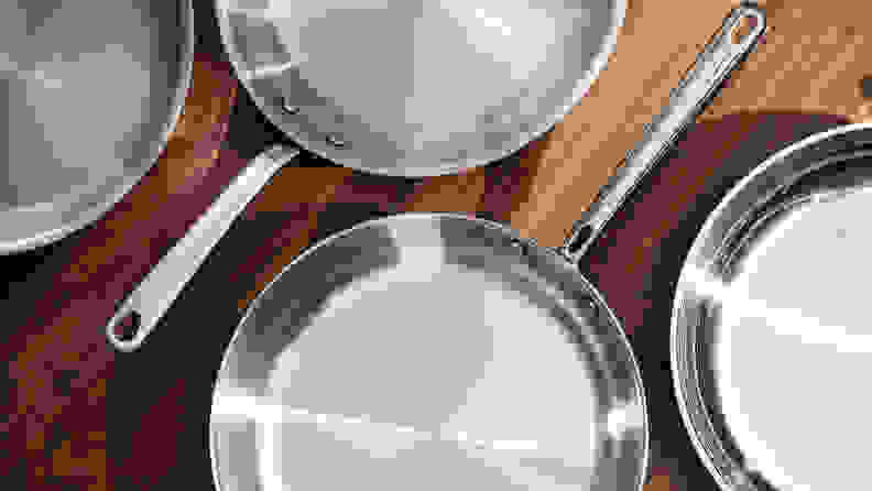 Four empty stainless steel skillets sit on a kitchen counter.