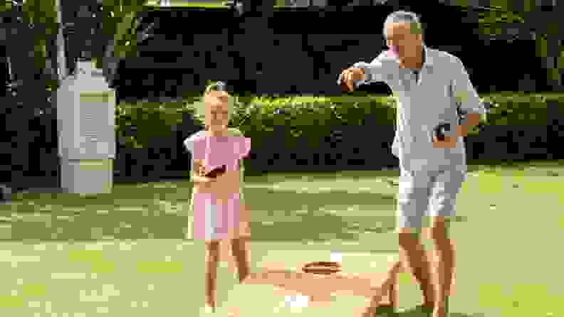A girl and her grandfather play cornhole