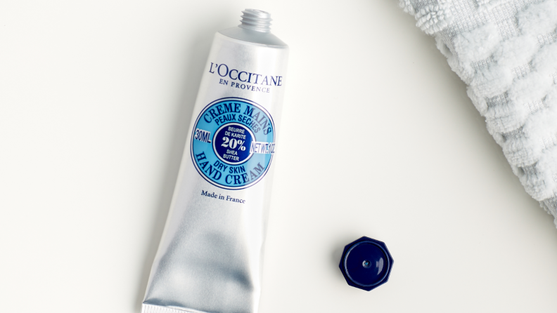 An image of an uncapped tube of L'Occitane hand cream next to a towel in gray.