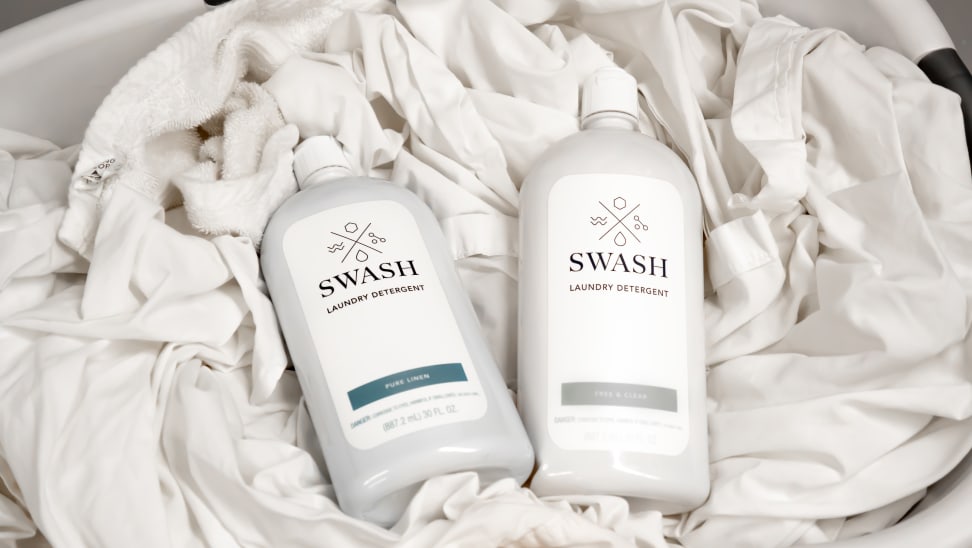 Two bottles of Whirlpool's Swash detergent, lying on a pile of white sheets.