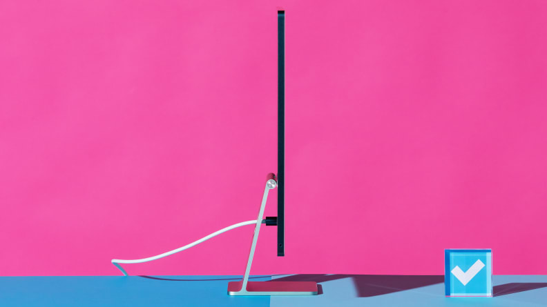 A profile view of an all-in-one iMac desktop computer standing on a blue surface against a hot pink background