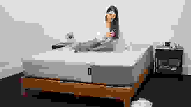 Person smiling at phone while on top of mattress.