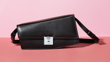 A black leather bag sitting on a pink surface with a pink background.