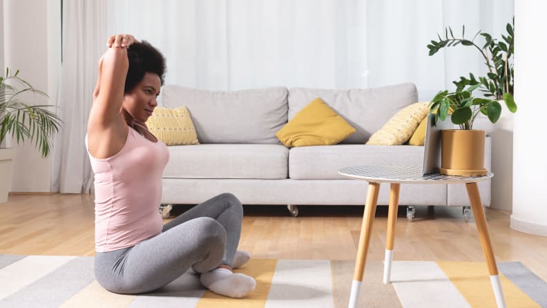 A woman stretching on the floor in front of a laptop.