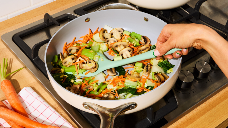 Person cooking colorful veggies in a nonstick pan while preparing one of the HelloFresh recipes at home.