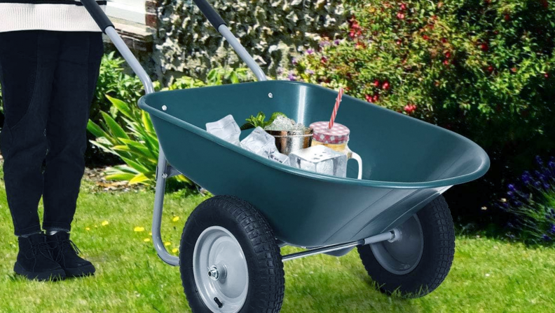 A close-up shot of the Goplus wheelbarrow being pushed across the lawn.