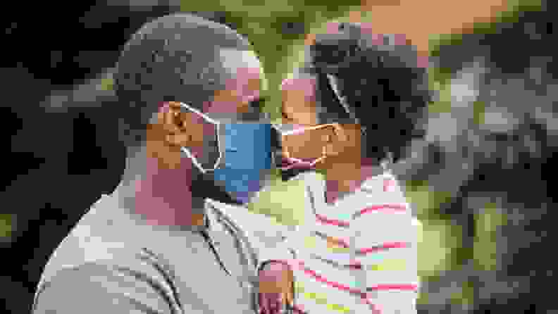 A dad and daughter touch noses while wearing masks.