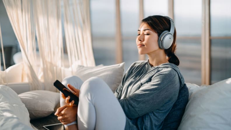 a person sits on a couch, leaned back wearing headphones and meditating