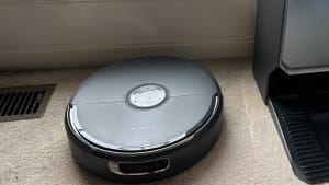 Black Narwal vacuum and docking station on a tan floor.