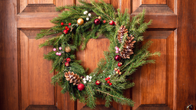 A wreath decorated with winter berries and pinecones against a natural wood door.