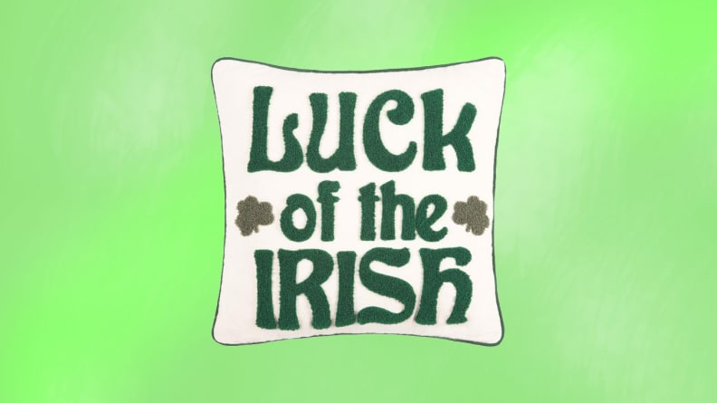 A white pillow with Luck of the Irish stiched on in front of a green background.