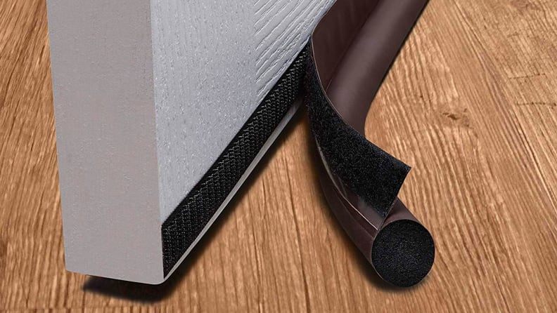 The bottom edge of an open door, slightly ajar, with a strip of hook and loop fastener running across it, parallel to the ground. A small foam roll is attached via a flap with the other side of the hook and loop fastener.
