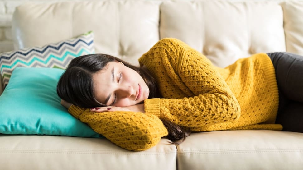 a woman naps in a yellow sweater on her beige couch