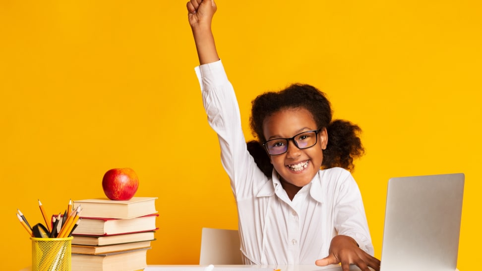 A child in front of a laptop with their hand raise up in the air in excitement.