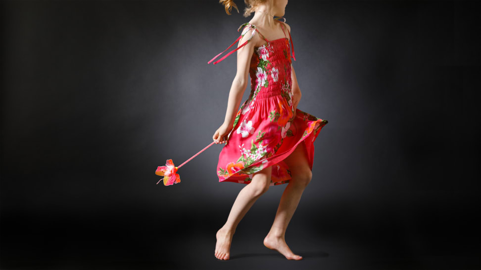 A young girl wearing a pink sundress and dancing with a wand