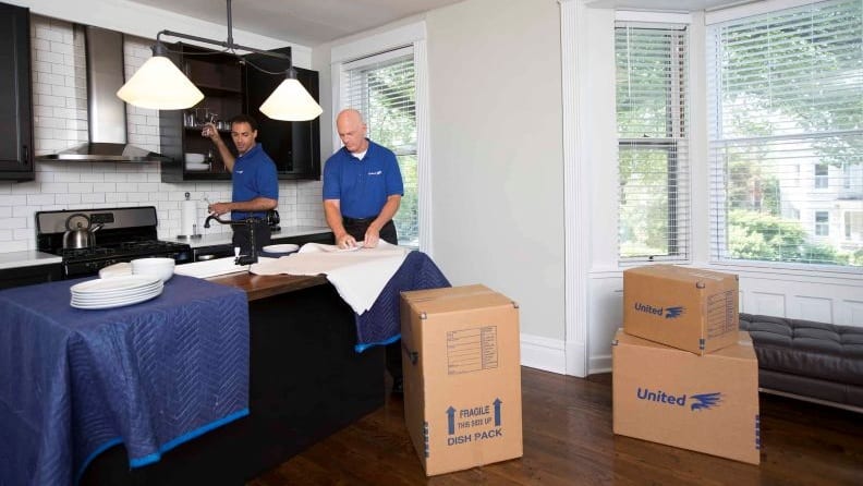 Two movers packing plates and wine glasses