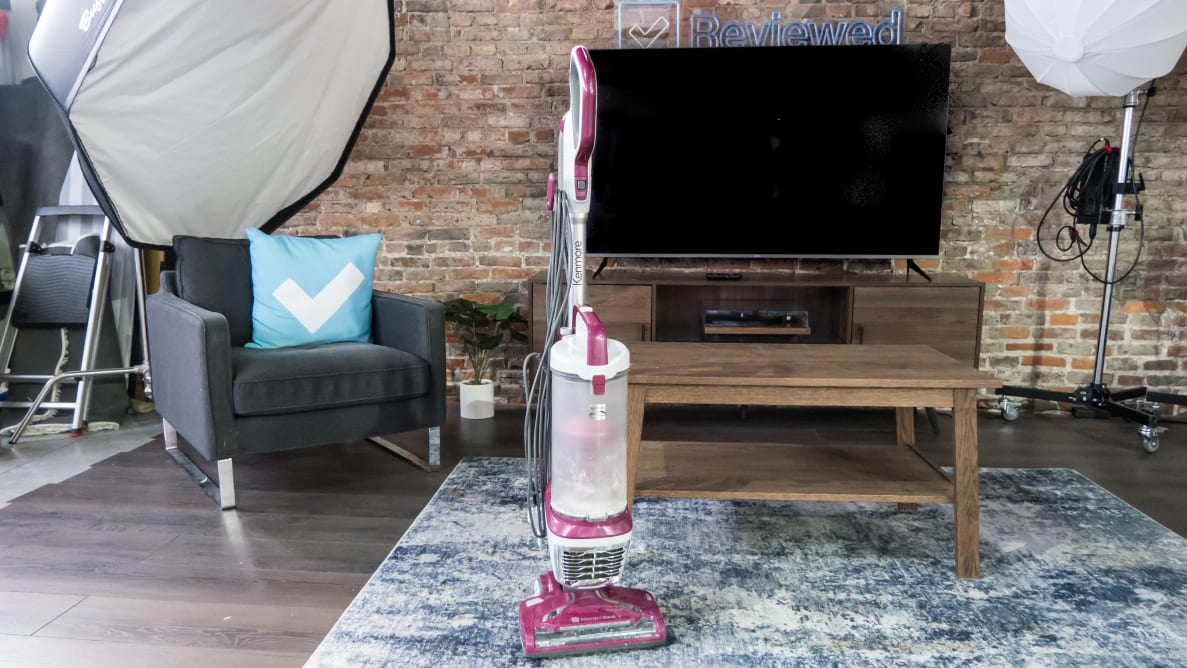 A red upright vacuum stands on a blue carpet