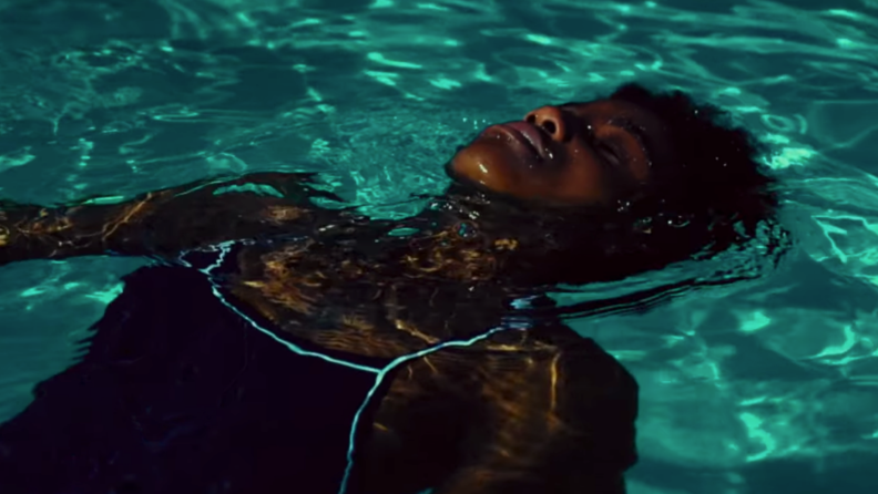 A still from the film "A Love Song for Latasha" featuring a Black woman in a pool staring upward toward the sky.