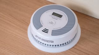 A round, white smoke detector sits on a wood background