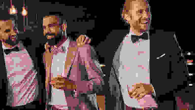 Three men wearing colored tuxedos and holding cocktails.