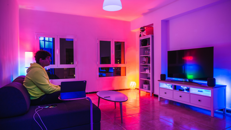 Person sitting in living room on the couch watching TV with bright pink, purple, and orange neon lights saturating the entire room