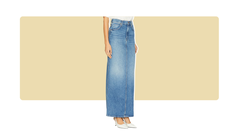 A model wearing a columnar blue denim maxi skirt with a front seam. The skirt is paired with white shoes.