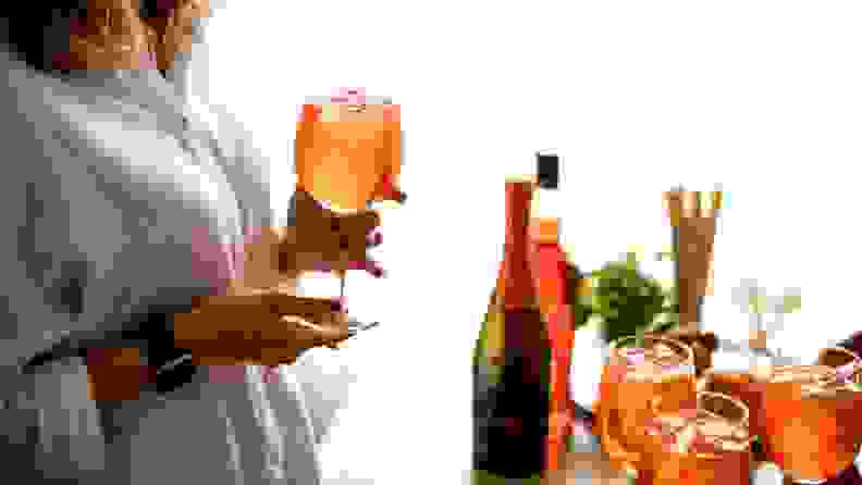 An individual holds a glass of chilled wine. Three more glasses are prepared in front of them, along with two wine bottles.